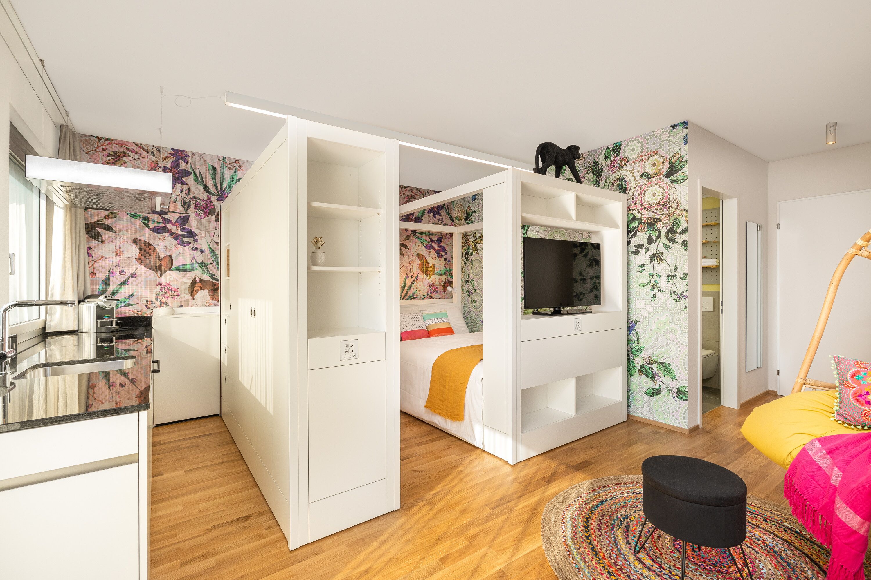 Une chambre compacte et moderne, dotée d’un lit, d’un téléviseur intégré et d’une petite kitchenette.