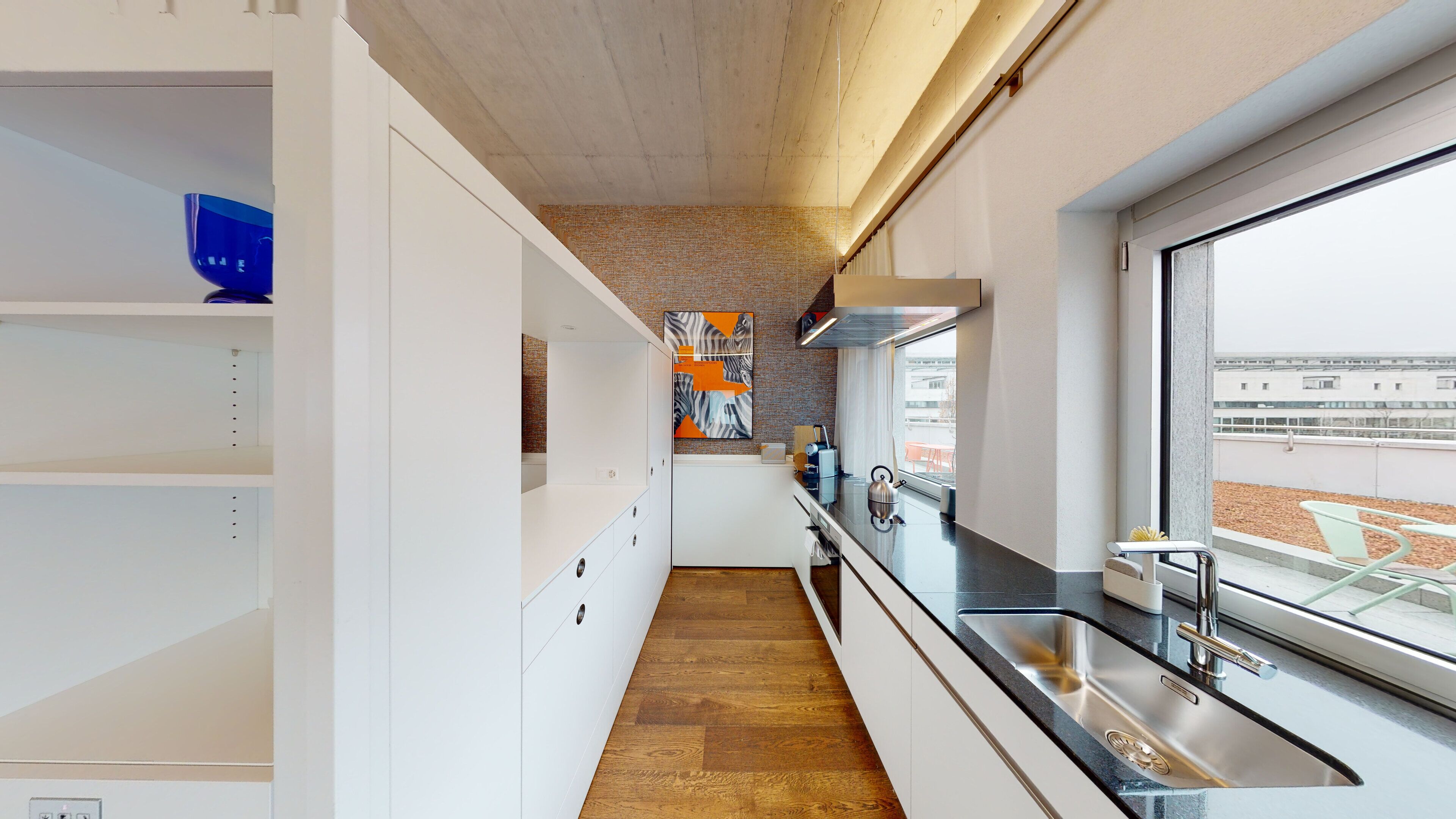 Une cuisine moderne avec des meubles blancs, un plancher en bois et une grande fenêtre donnant sur la ville.