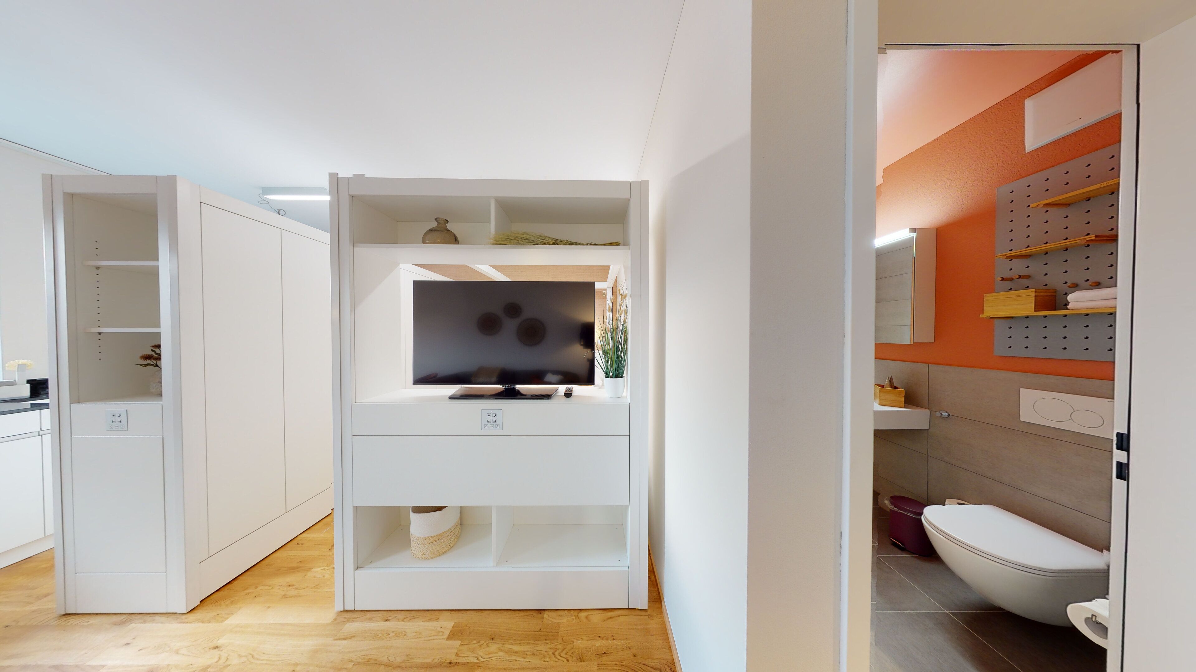 A modern kitchen with white cabinetry, a built-in TV, and a wooden floor.