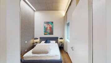 Een smalle hotelkamer met een bed, twee nachtkastjes, een wanddecoratie en een raam.