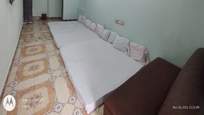A room with a long bed, a ceiling fan, an air conditioner, and a television mounted on the wall. - Sri Sivalakshmi AC Guest House (Vriddhachalam)
