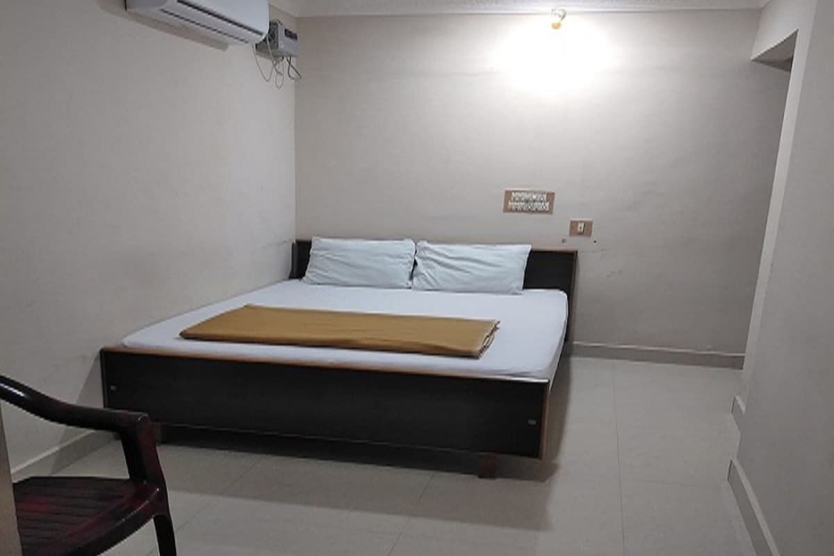 A bedroom with a bed, a chair, an air conditioning unit, and a ceiling light.