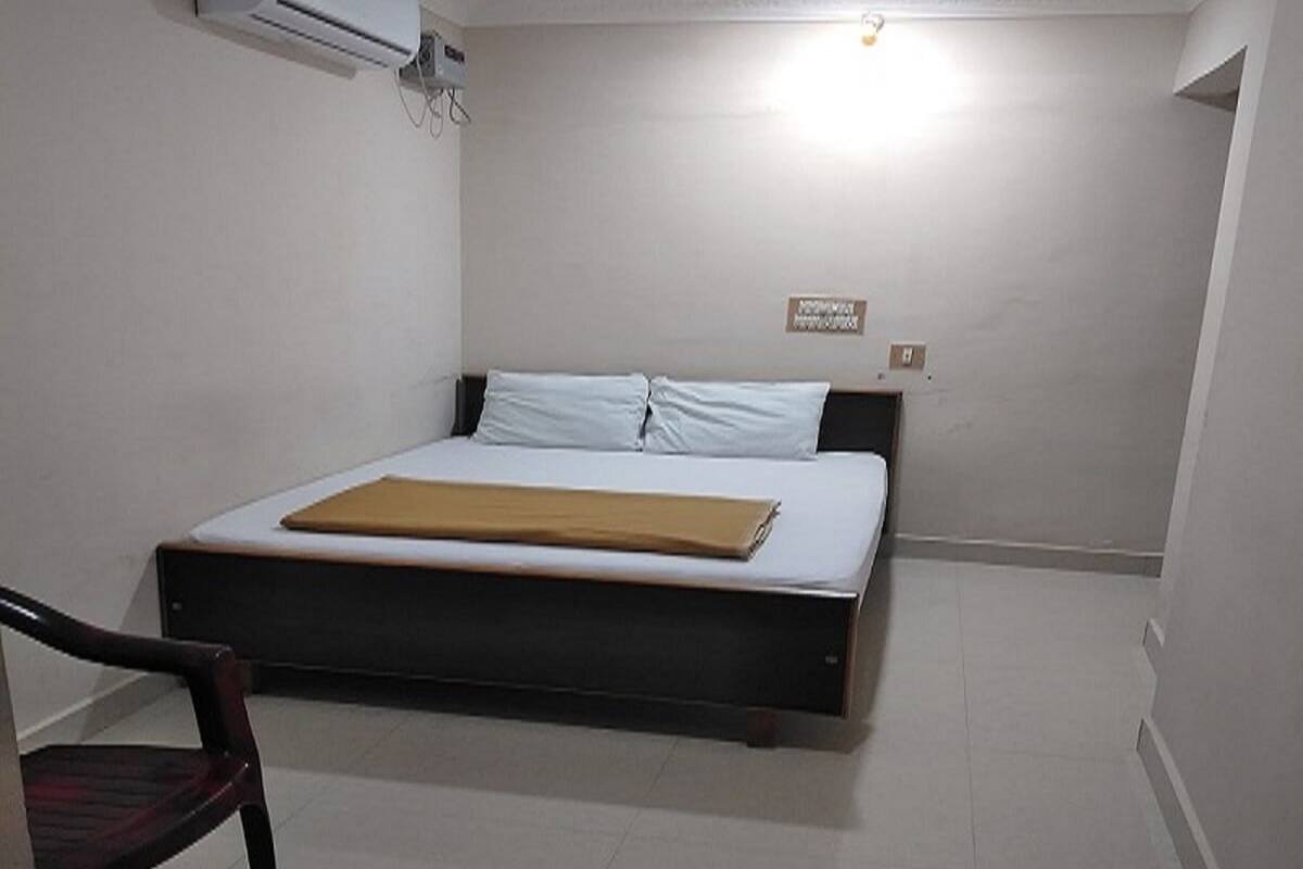 A bedroom with a bed, a chair, an air conditioning unit, and a ceiling light.
