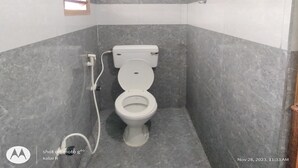 A small, modern bathroom with a toilet, a shower area, and a handrail. - Sri Sivalakshmi AC Guest House (Vriddhachalam)