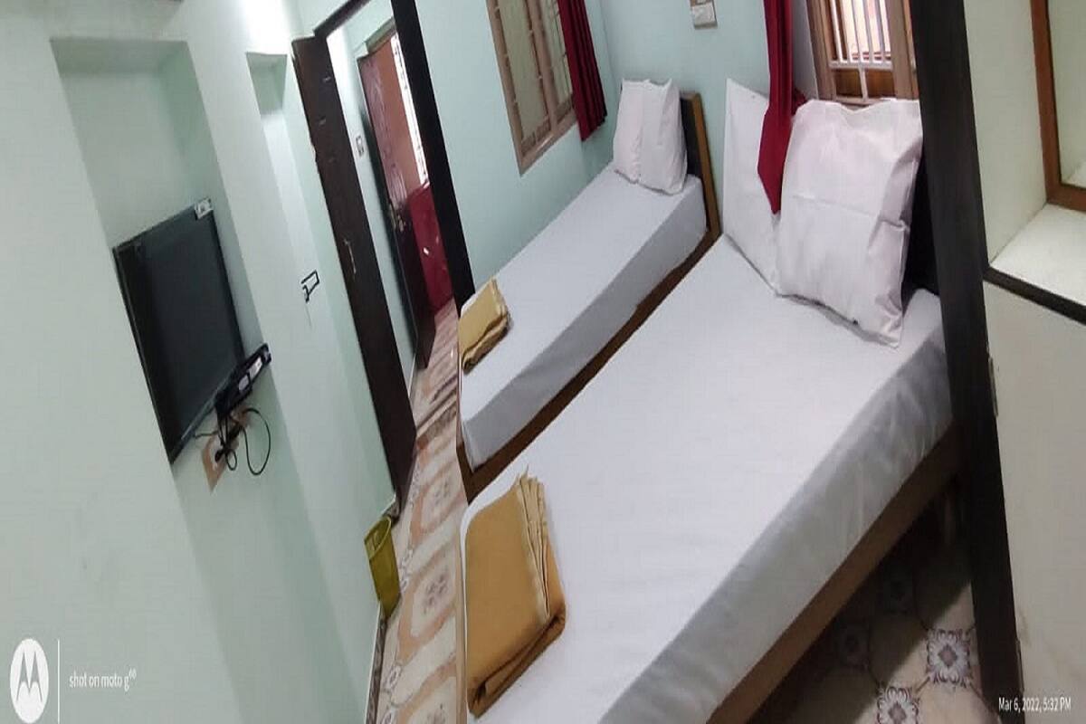 A room with two single beds, a small table, a TV mounted on the wall, and an air conditioning unit.