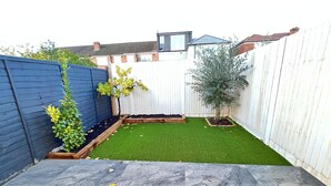 A backyard with artificial grass, a blue fence, and a white fence. - Stunning 1-bed Studio in Greenford (Greenford)