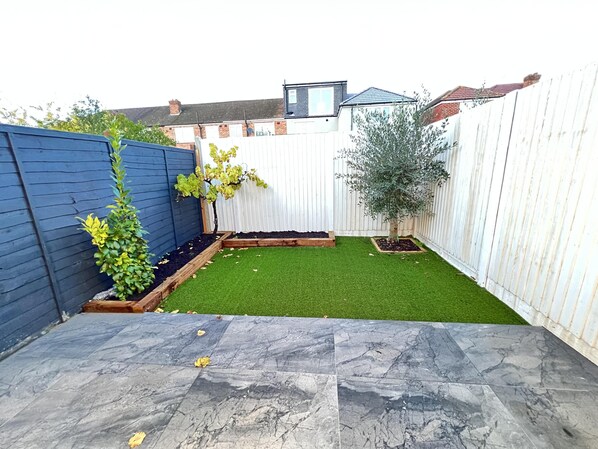 A backyard with artificial grass, a blue fence, and a white fence.