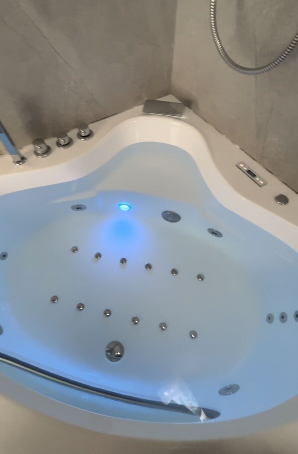 Un baño moderno con una bañera independiente, un cabezal de ducha manual y un panel de control visible.