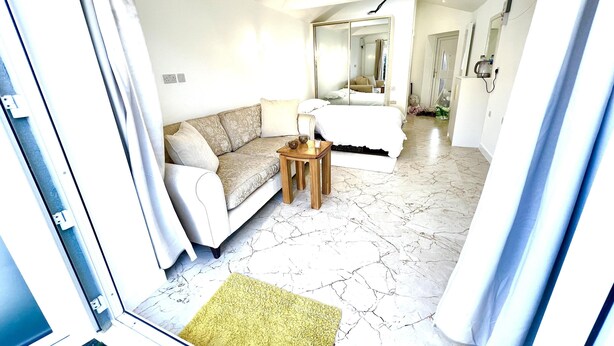 A hotel room with a sofa, a small wooden table, a bed, and a bathroom visible through an open door. - Stunning 1-bed Studio in Greenford (Greenford)