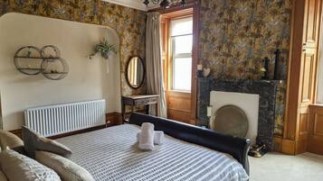 Una camera da letto con un letto grande, un termosifone, uno specchio, un camino e una finestra con tende.