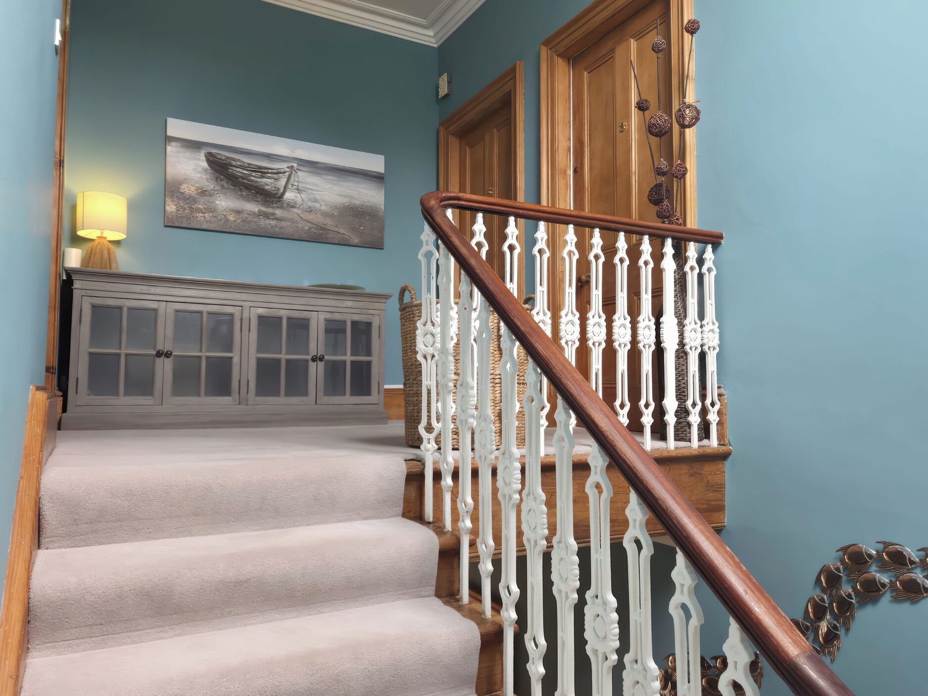 A staircase with white balusters and a wooden handrail leading to a door with a basket on the wall.
