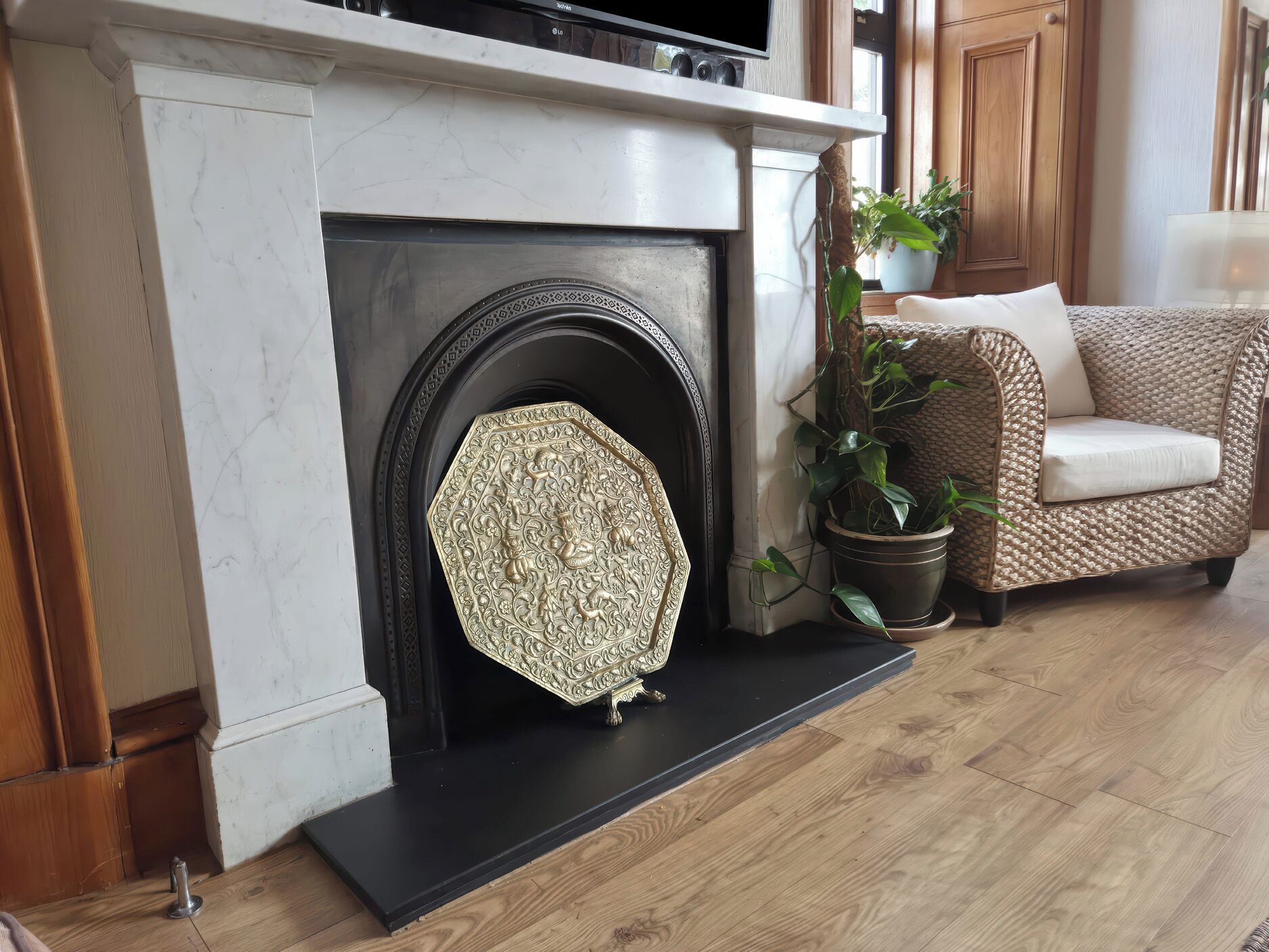 Una chimenea con una pantalla decorativa, un sofá de mimbre y una planta en maceta en una sala de estar.