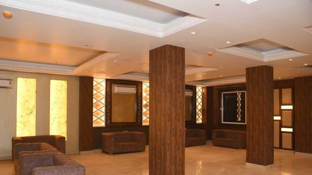 A spacious lobby with a marble floor, large wooden columns, and a seating area with cushioned sofas. - SWARN BHOOMI (Kanpur)