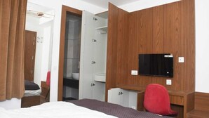 A hotel room with a bed, a desk, a TV, and a wardrobe. - SWARN BHOOMI (Kanpur)