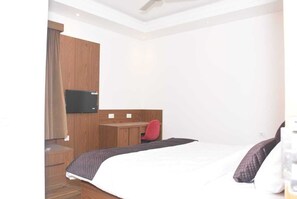 A hotel room with a bed, a desk, a chair, a TV, and a wardrobe.