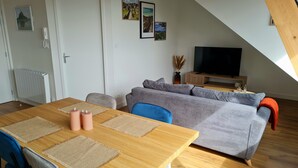 Una sala de estar moderna con una mesa de comedor de madera, un sofá gris y un televisor sobre un mueble de madera.