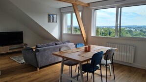 Una sala de estar moderna con una mesa de comedor, un sofá gris y un televisor.