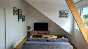 Una sala de estar moderna con una viga de madera en el techo, un sofá gris, un televisor y cuadros en las paredes.