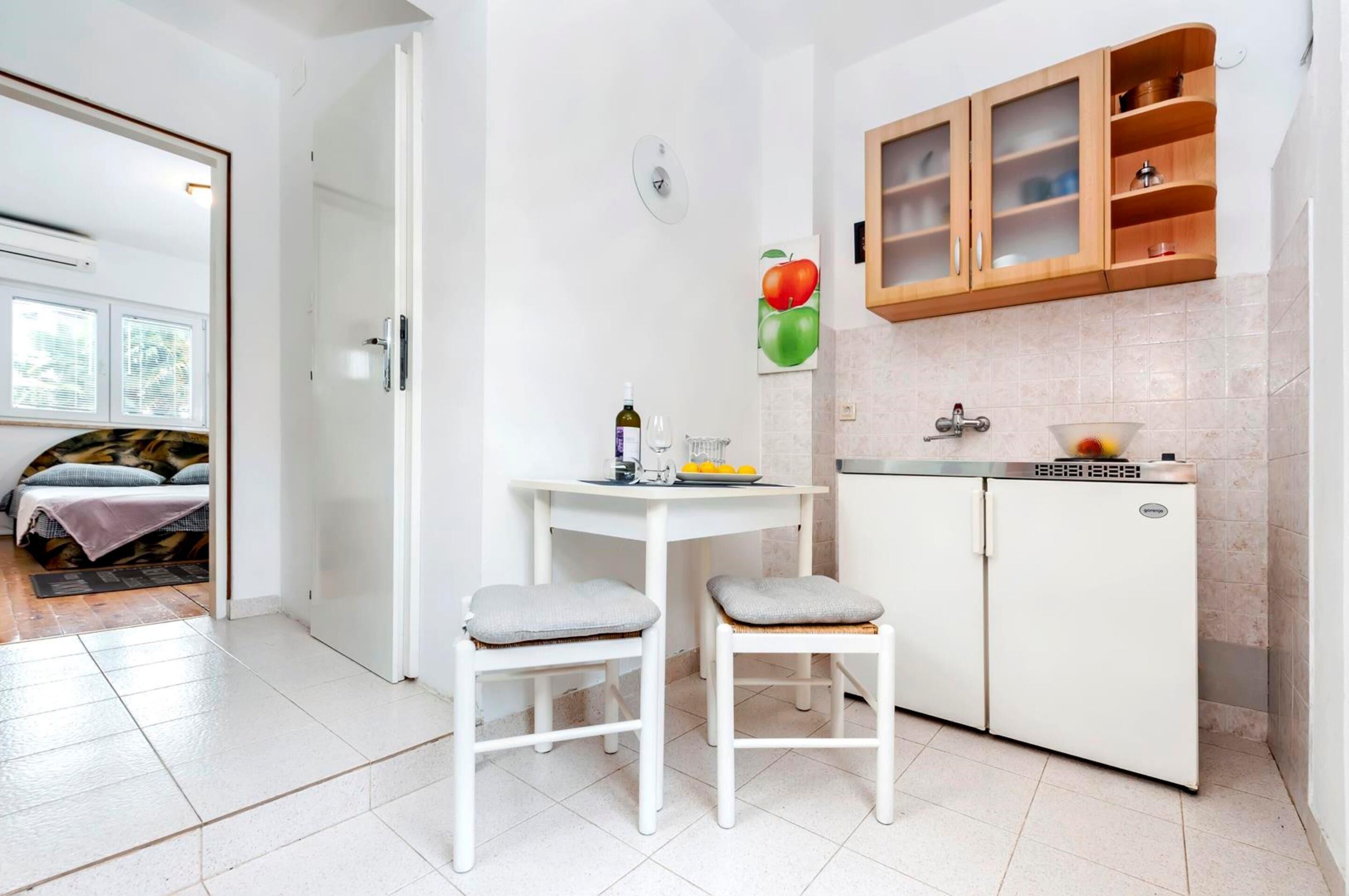 A compact kitchen with a white refrigerator, a small table with two stools, and wooden cabinets above the sink.