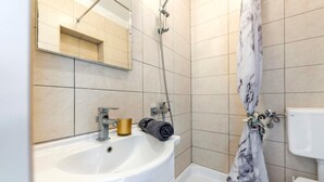 Kylpyhuone, jossa on valkoinen pesuallas, peili, suihku ja wc.