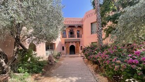 A courtyard with a paved walkway leading to a building with traditional architecture, surrounded by lush greenery and flowering plants. - Au Riad De La Palmeraie - Marrakech  (Marrakech)