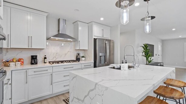 Una cocina moderna con armarios blancos, una isla de mármol, electrodomésticos de acero inoxidable e iluminación colgante.