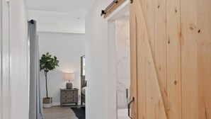 Un pasillo con una puerta de madera, una planta, una mesita de noche y una lámpara.