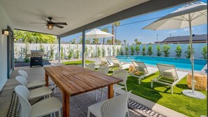 Un patio con mesa y sillas de madera, una piscina y sillones de descanso.