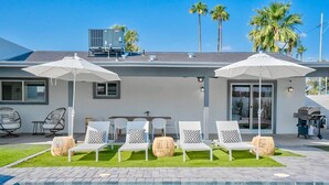 Un área de piscina moderna al aire libre con sillones reclinables blancos y sombrillas, una piscina azul cristalina y un césped bien cuidado.