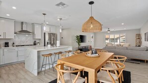 Una cocina moderna con armarios blancos, una isla central y un comedor con sillas y mesa de madera.