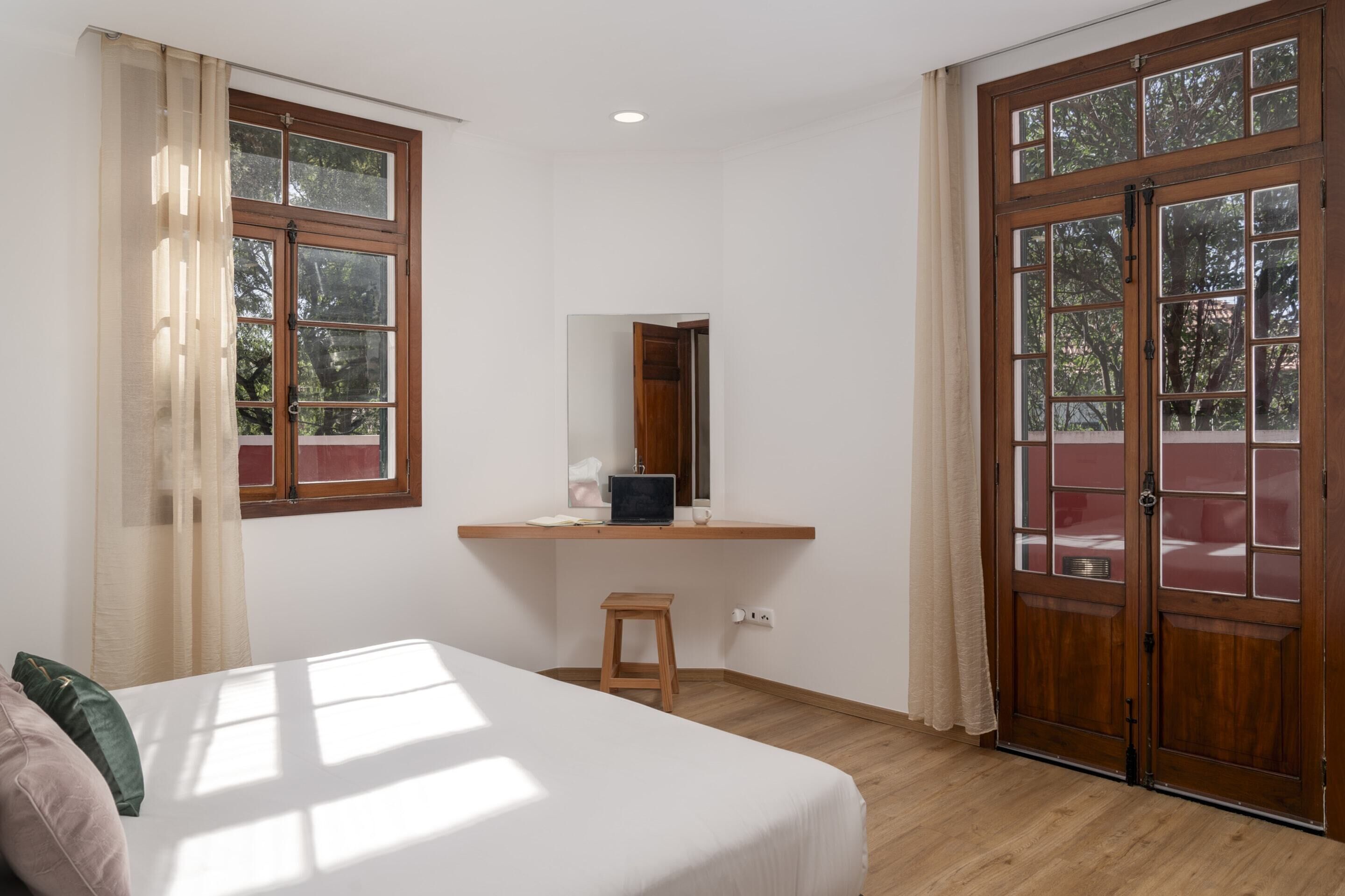 A bedroom with a bed, a desk, and a window.