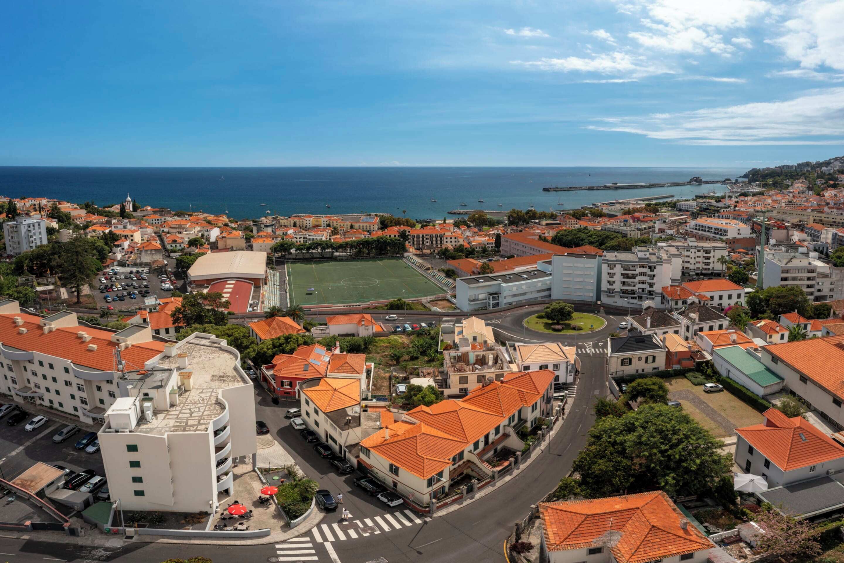 Une ville côtière aux bâtiments aux toits rouges, dotée d’un terrain de sport et offrant une vue dégagée sur la mer.