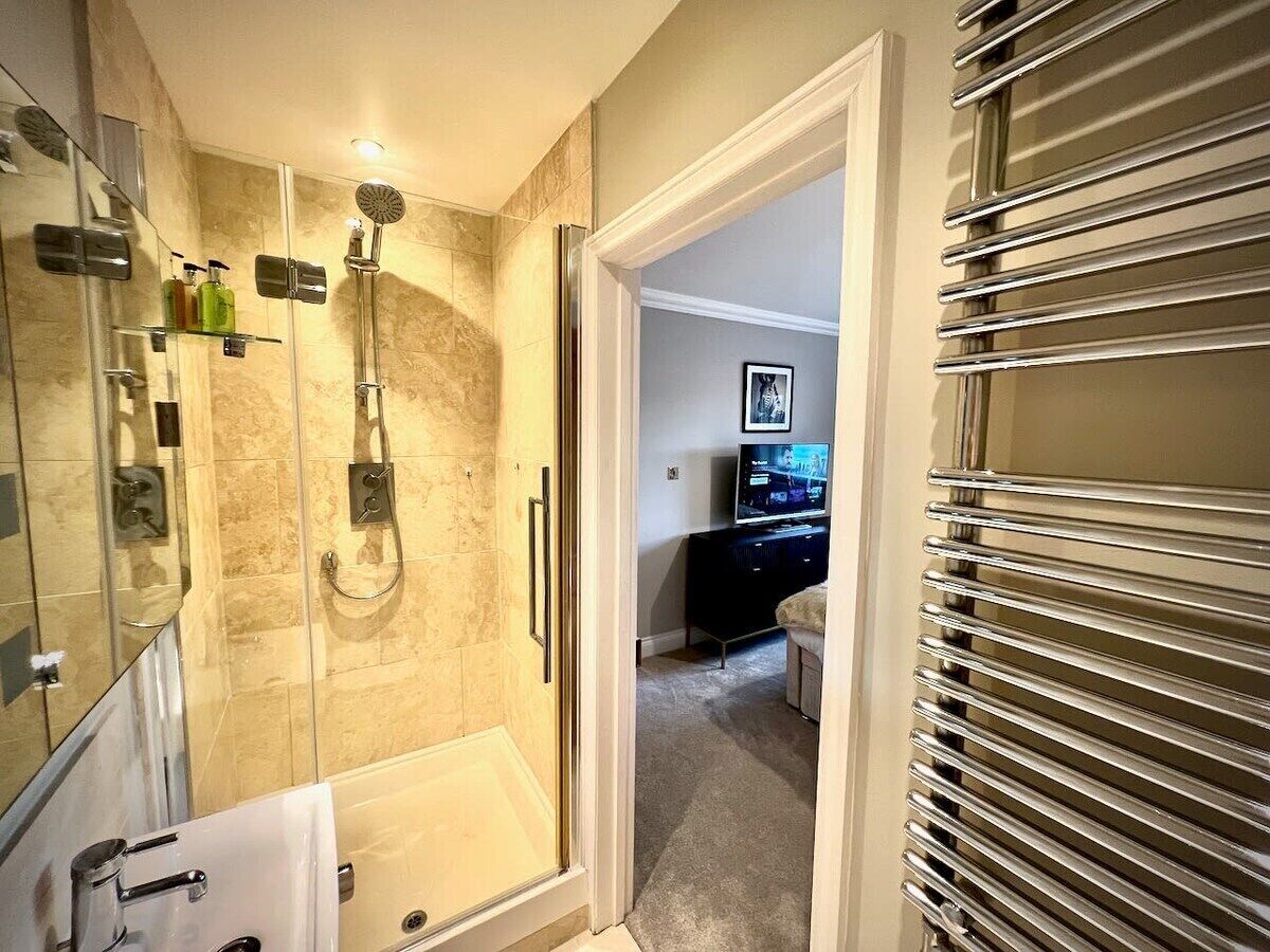 Een moderne badkamer met een douchecabine van glas, een wastafel met spiegel en een inloopkast met televisie.