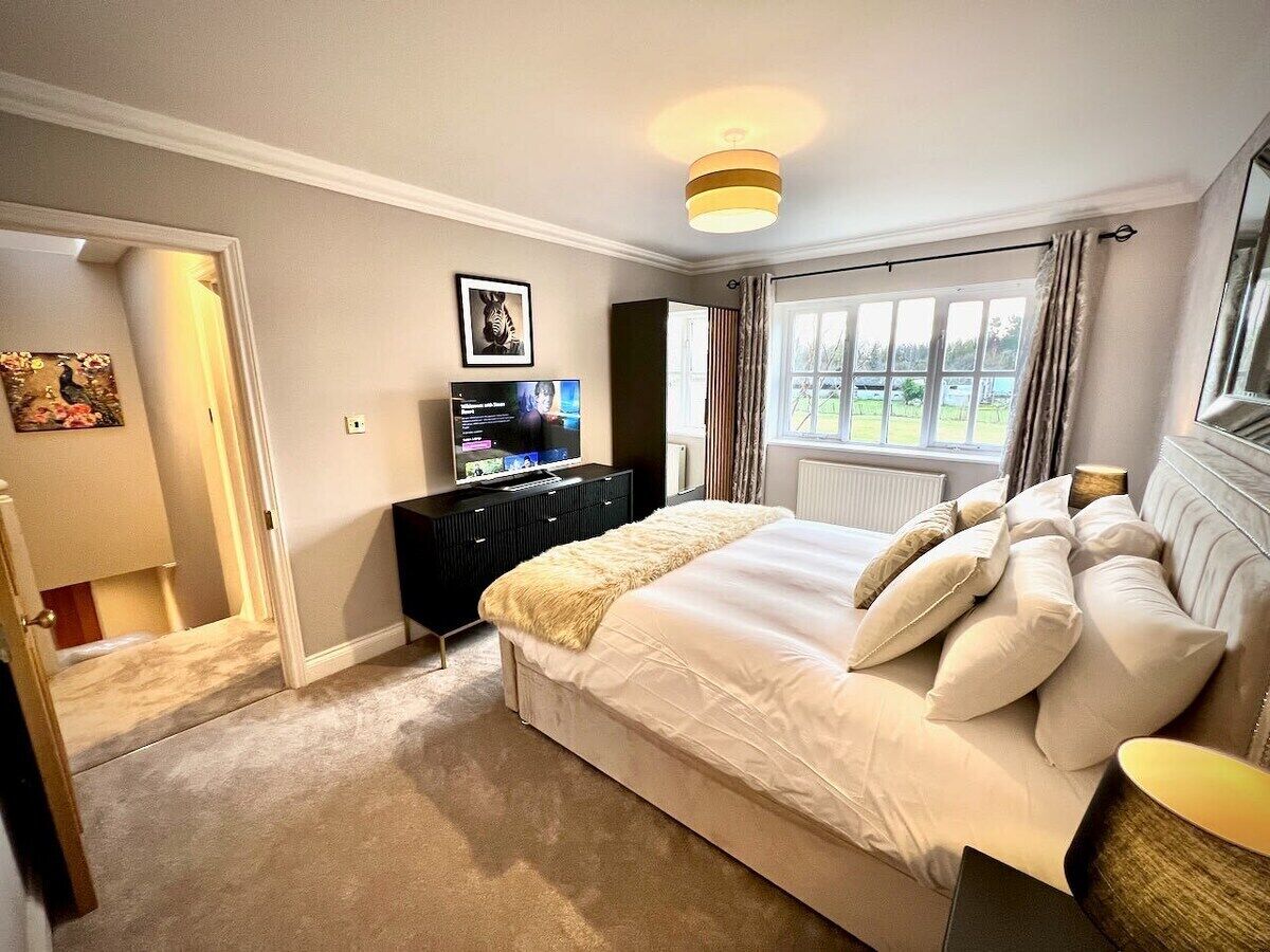 A bedroom with a large bed, a TV, a dresser, and a window with curtains.