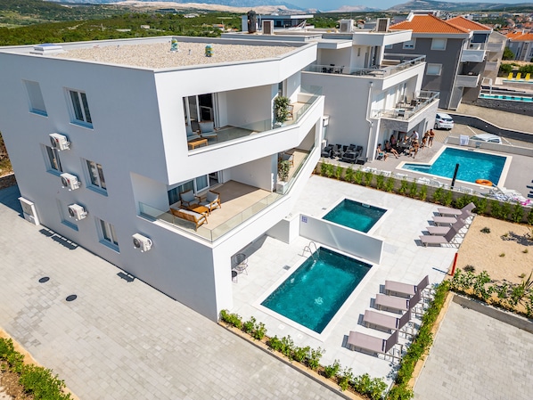 A modern multi-story building with a rooftop terrace, a swimming pool, and outdoor seating areas.