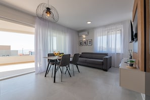 A modern living room with a dining area, a grey sofa, and a TV mounted on the wall.
