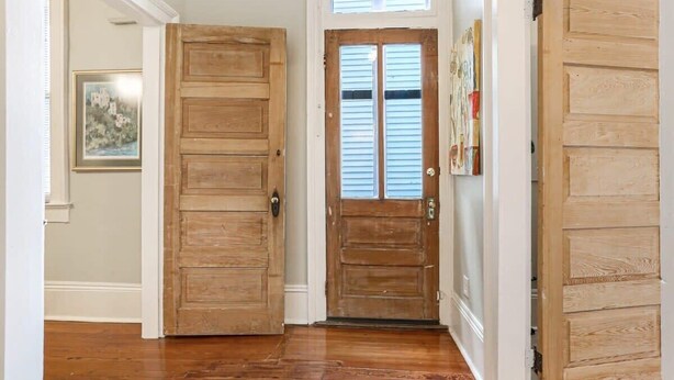Un pasillo con puertas de madera, un cuadro en la pared y un ventanal sobre la puerta.