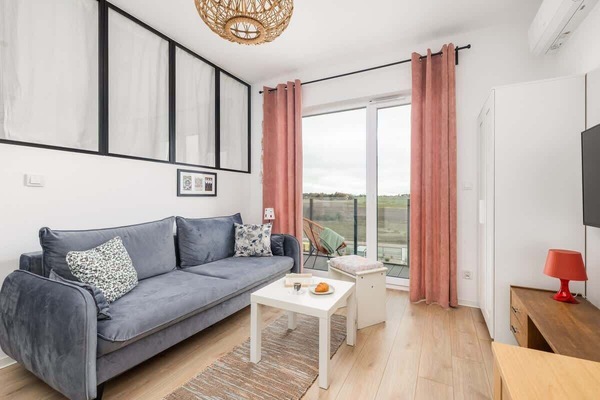 A bright living room with a gray sofa, a white coffee table, and large windows with pink curtains.