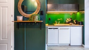 A modern kitchen with a green backsplash, white cabinets, and a wooden shelf with a mirror and decorative items. - Cozy Studio in the Center | Balcony | Close to Train Station (Katowice)