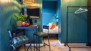 A compact room with a desk, two chairs, a television, a hanging light fixture, a bed with pillows, and a coat rack. - Cozy Studio in the Center | Balcony | Close to Train Station (Katowice)