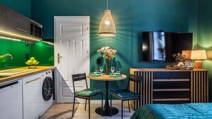 A compact kitchen with a washing machine, a dining area with a table and chairs, a TV mounted on the wall, and a bed with a green blanket. - Modern Studio in the Center | 600 m to the Market, Close to the Station (Katowice)