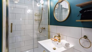 A modern bathroom with a glass-enclosed shower, a white sink with gold fixtures, a mirror with a gold frame, and a towel rack.