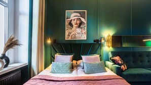 A bedroom with a large bed, a green upholstered sofa, and a painting on the wall.