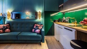 A modern living room with a sofa and a kitchen area with a green wall and wooden countertop.