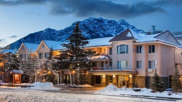 Un hôtel situé au pied d’une montagne enneigée, avec un bâtiment principal doté d’une grande véranda et de nombreuses fenêtres.