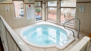 Un bain à remous dans une pièce aux murs carrelés, dotée de grandes fenêtres et d’une horloge bien visible.