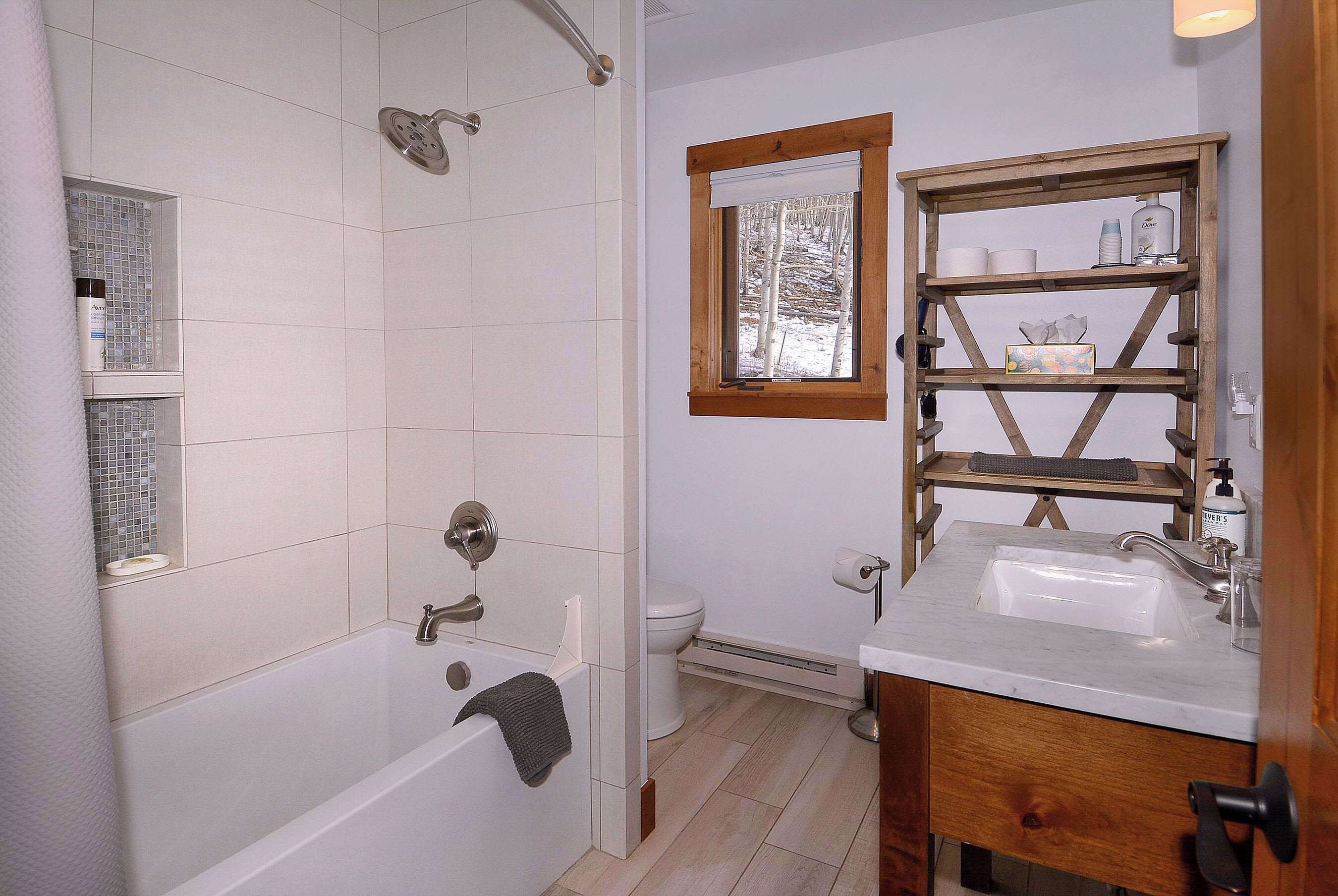 A bathroom with a bathtub, a toilet, a sink, and a window with a view of trees.