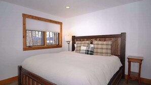 Une chambre à coucher avec un lit en bois, une fenêtre donnant sur des arbres et une table de chevet.