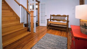 Un escalier en bois avec une rampe, un banc, un tapis et un meuble rouge.