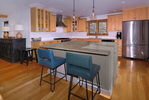 Una cocina moderna con armarios de madera, un refrigerador de acero inoxidable y una isla central con taburetes de bar.